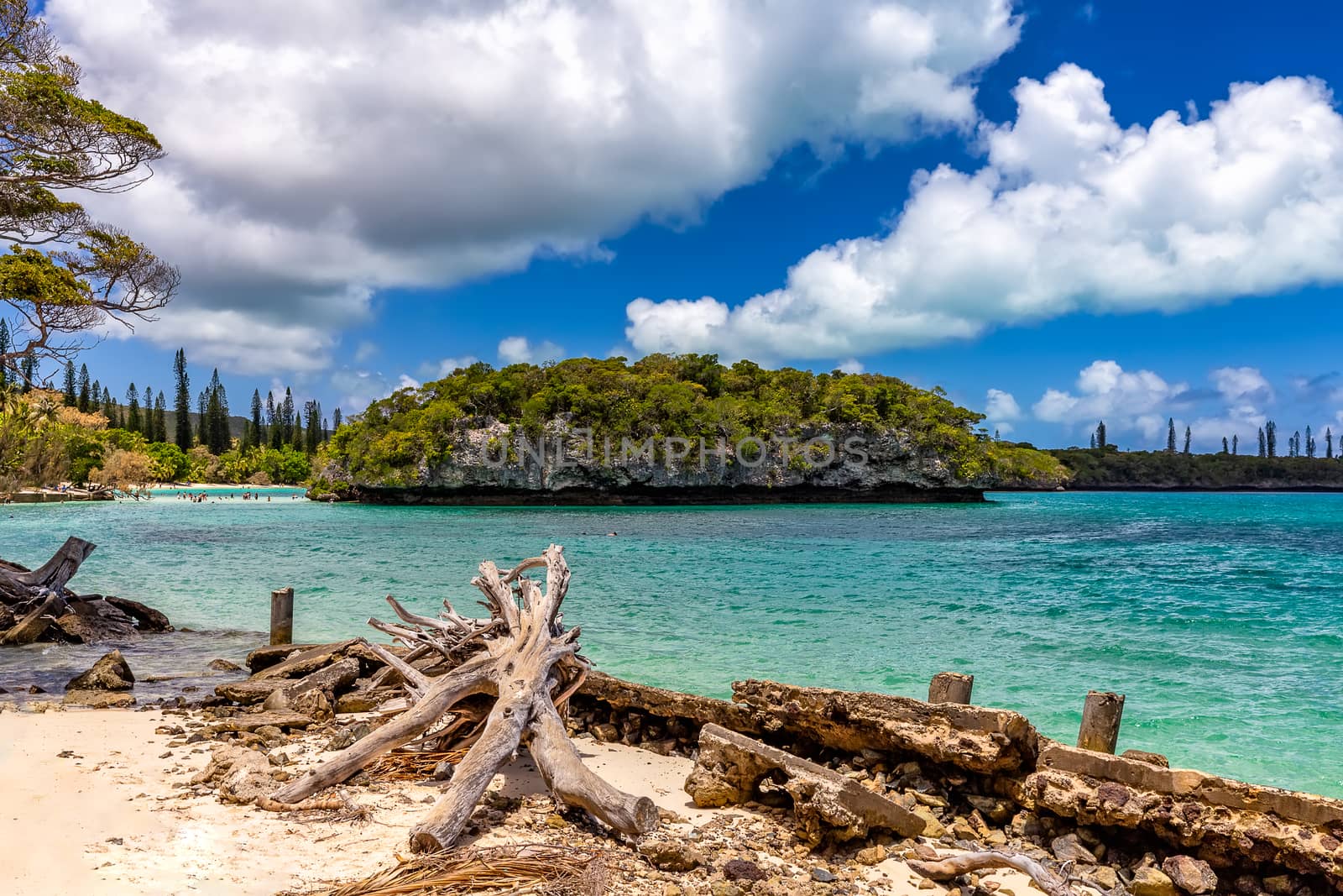 View of a tropical sandy shoreline with a massive rocky island, blue sky and clouds in the background.