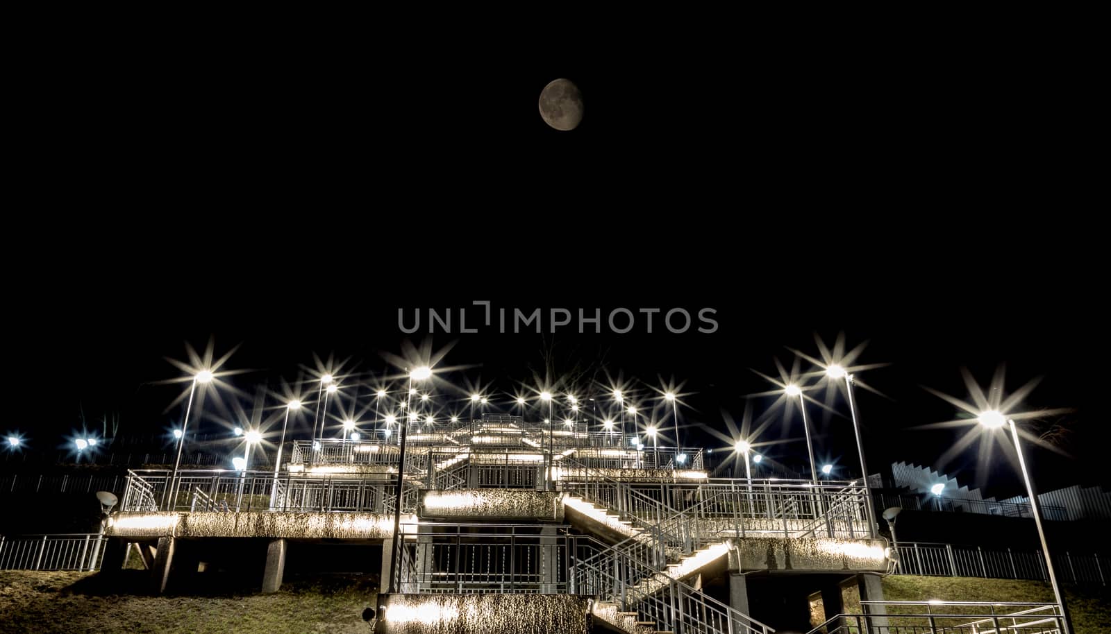 Night view of a staircase leading up to the top of the hill with the Moon above it and lights paving the way to the top. City of Barnaul, Siberia, Russia