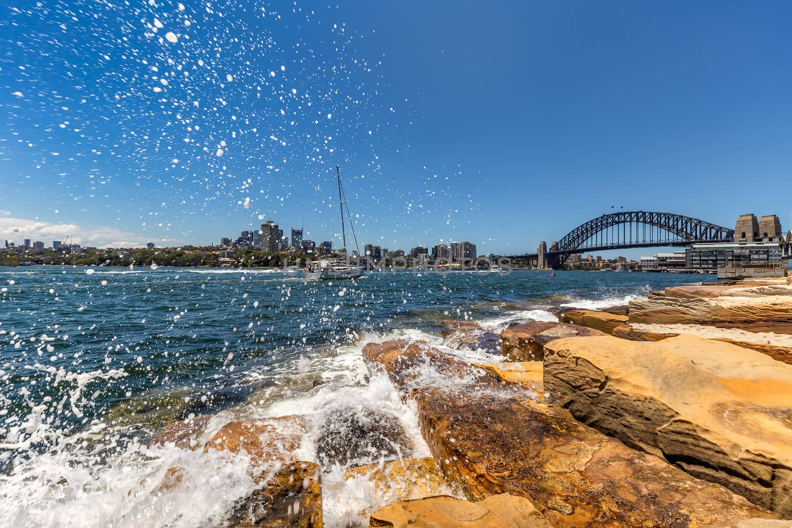 View of Harbor Bridge with a boat sailing in the distance and water splashing in the foreground in Sydney, Australia