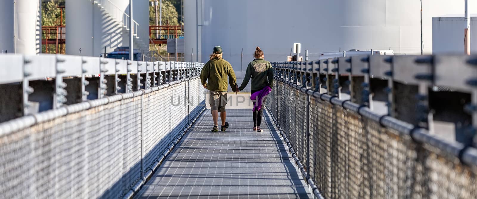Couple on the bridge holding hands and walking towards metal containers