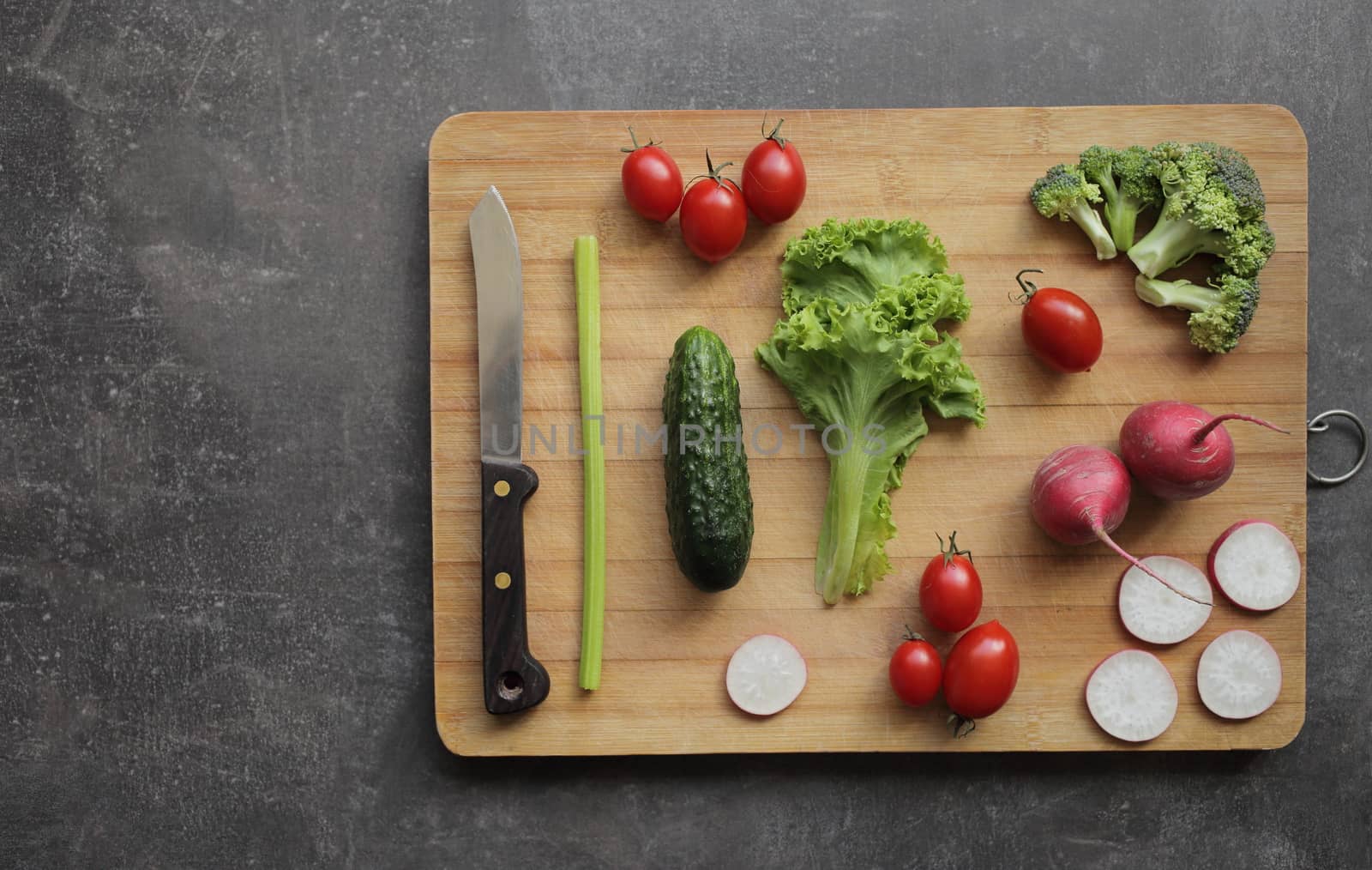 Fresh vegetables on a cutting board on a gray table Tomatoes, lettuce, broccoli, radish