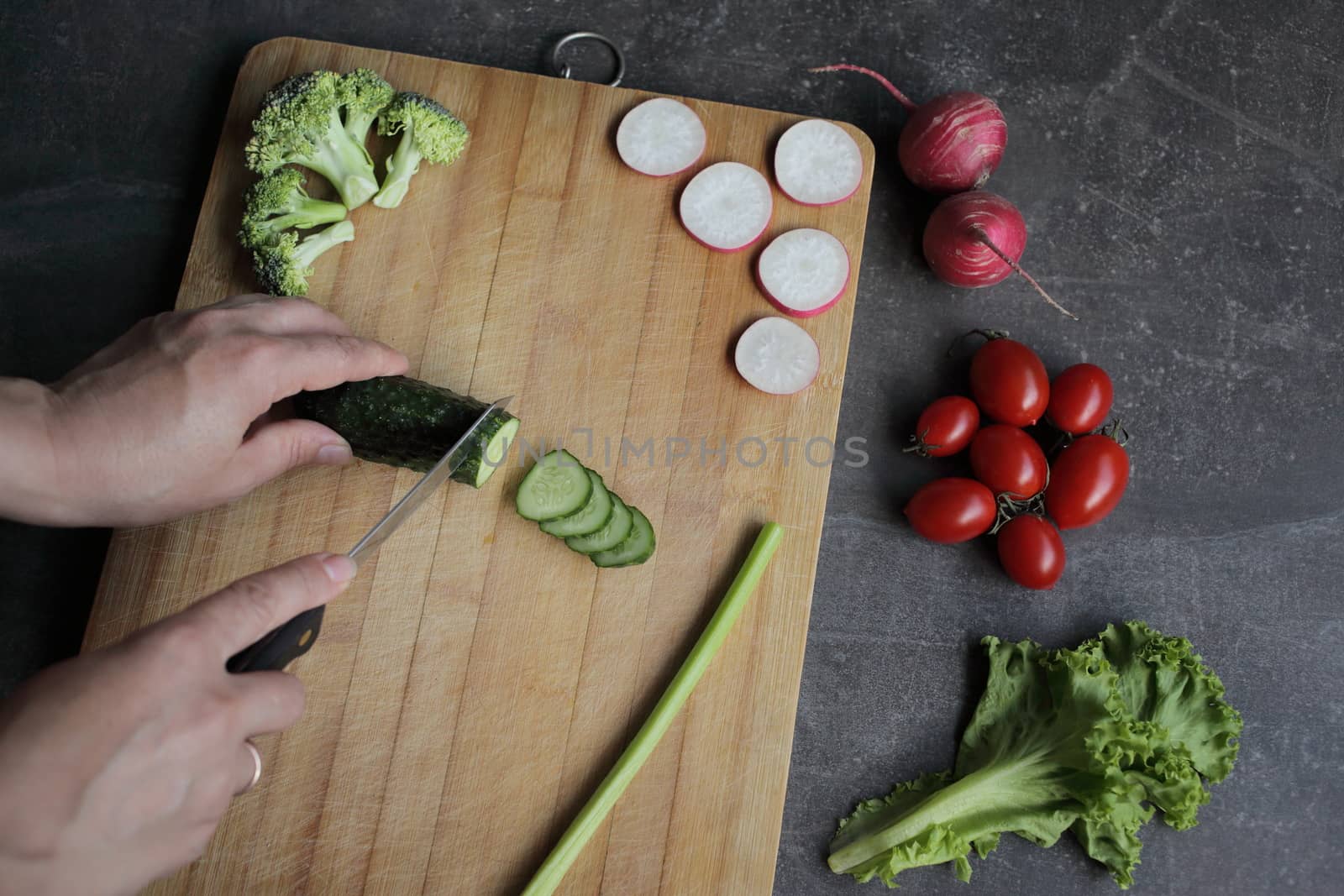 Hands cut a cucumber on a cutting board on a gray table. by selinsmo