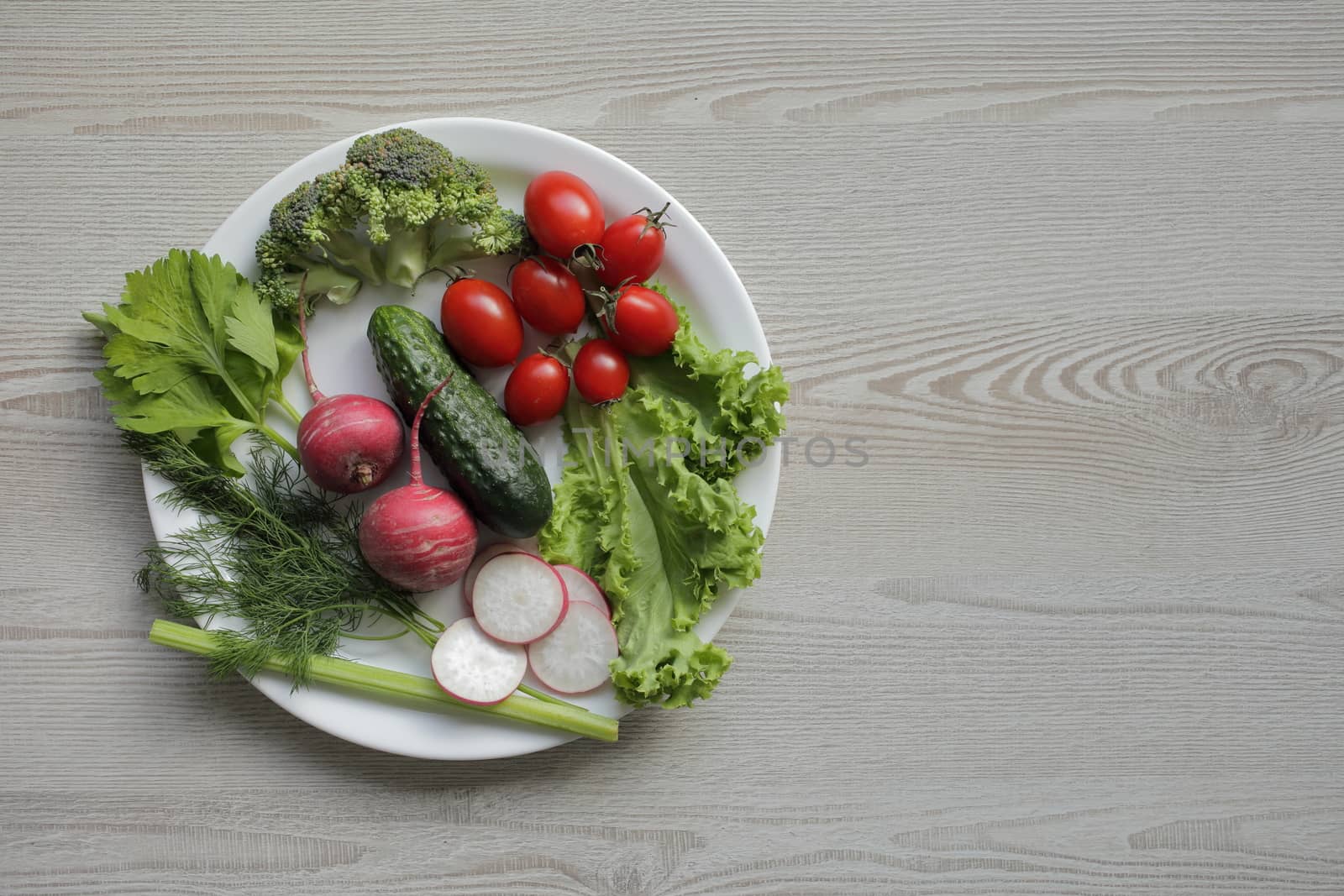 Fresh vegetables in a white plate on a light wooden table by selinsmo