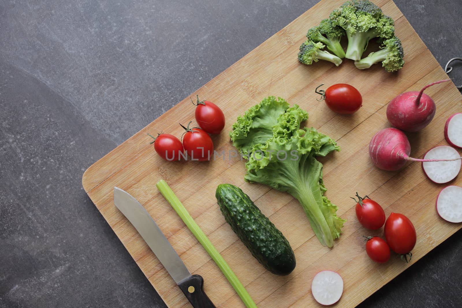 Fresh vegetables on a cutting board on a gray table Tomatoes, lettuce, broccoli, radish
