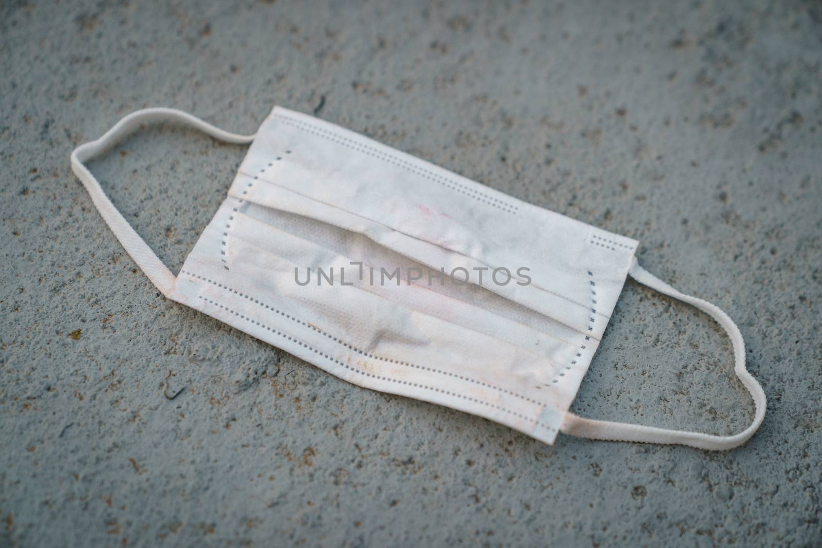 Used dirty face surgical mask dropped on the ground, selective focus center mask