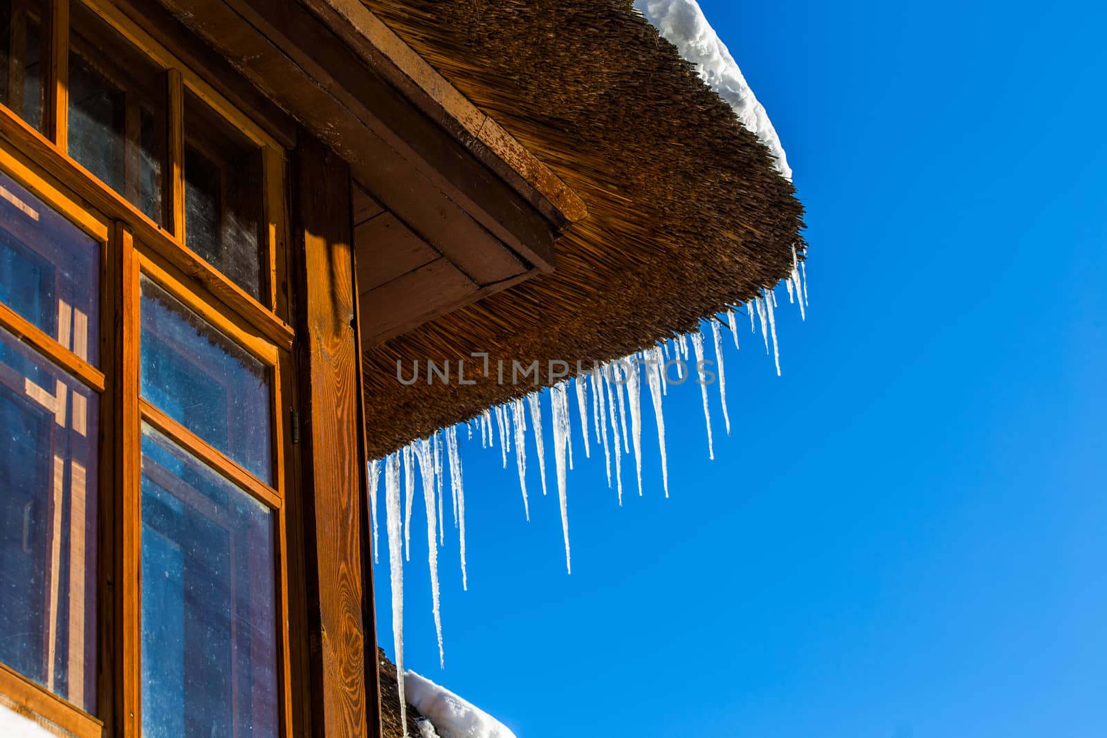 Icicles on straw roof corner of wooden rustic house with window