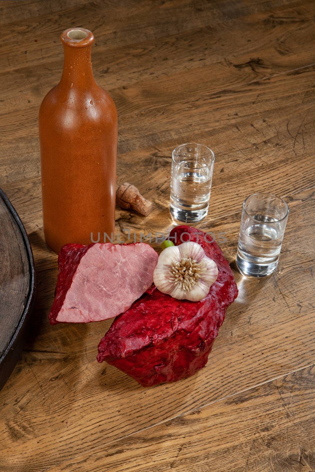 Ham sausage, ceramic bottle and glasses of vodka on a wooden desk