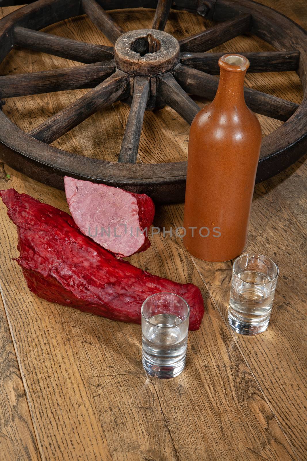 Ham sausage, ceramic bottle and glasses of vodka on a wooden desk