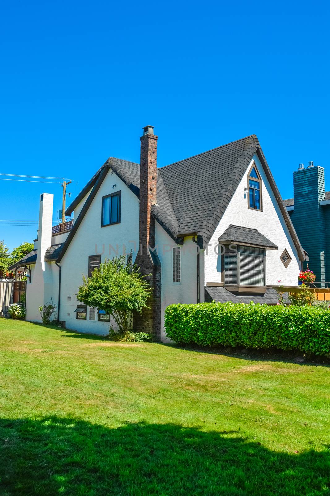 Old style family house with green lawn and hedgerow in front on blue sky background