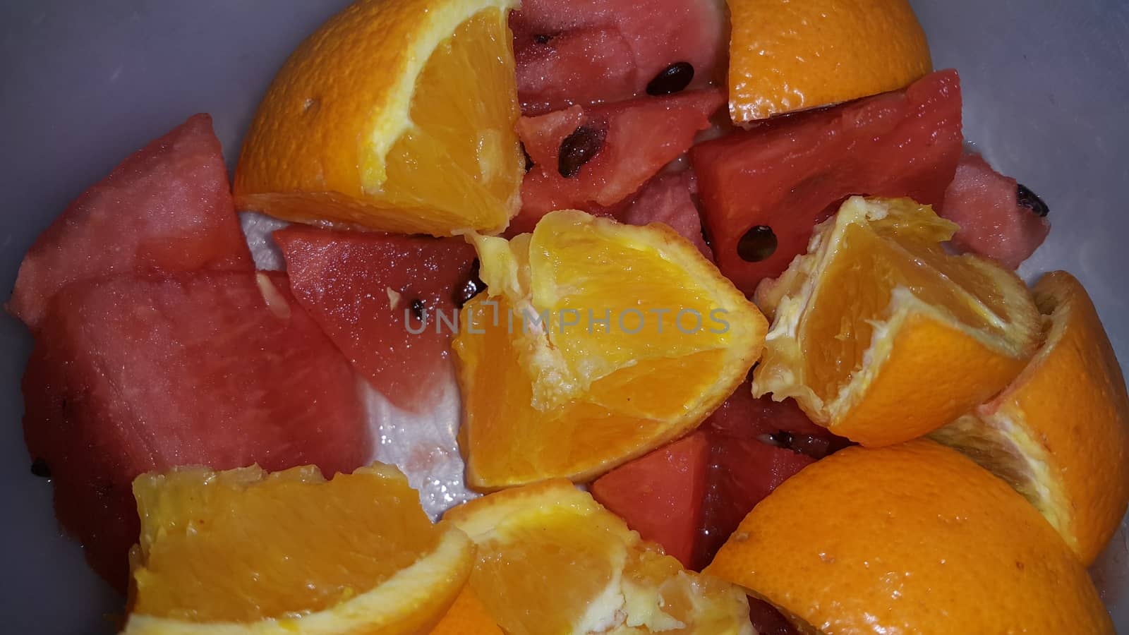 Closeup view of mixed fruits slices of oranges and red water melon served in a ceramic white plate. Water melon is sweet while oranges are citrus in taste