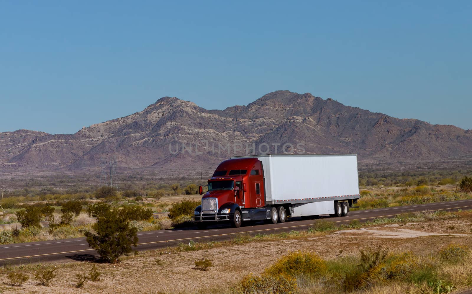 Classic big rig heavy duty long haul diesel semi truck with refrigerator semi trailer running on the road along mountains in USA