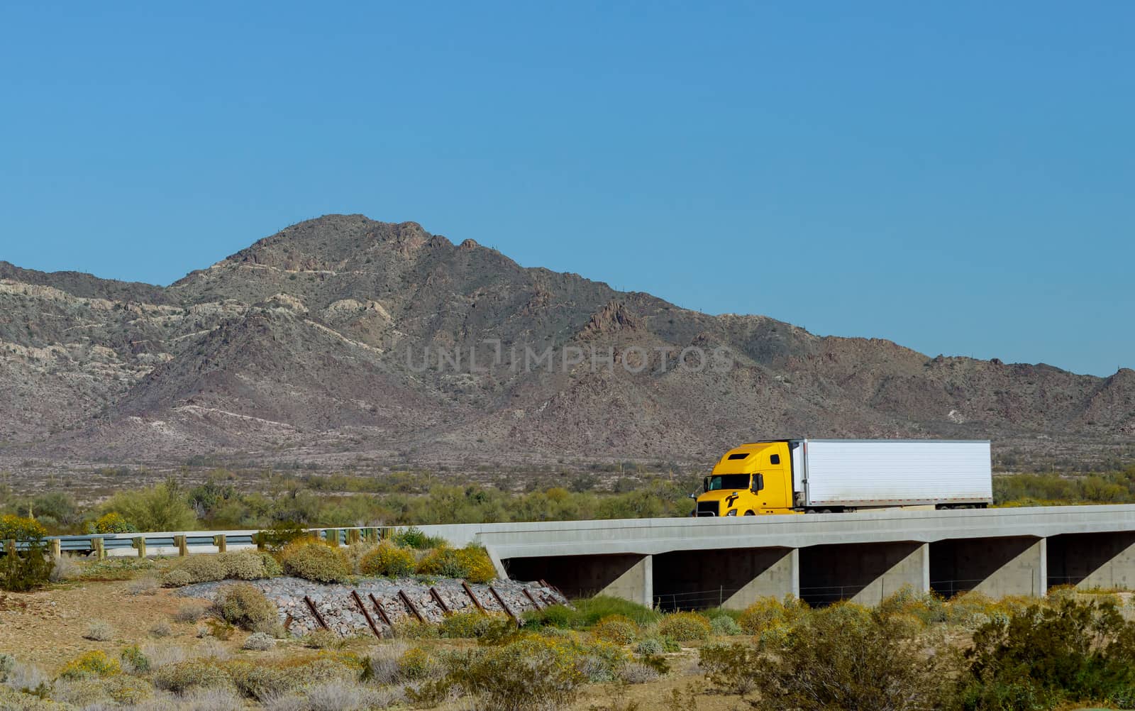 Big rig long haul semi truck with two flat bed semi trailers transporting on the winding road with bridge around the mountain rock in USA