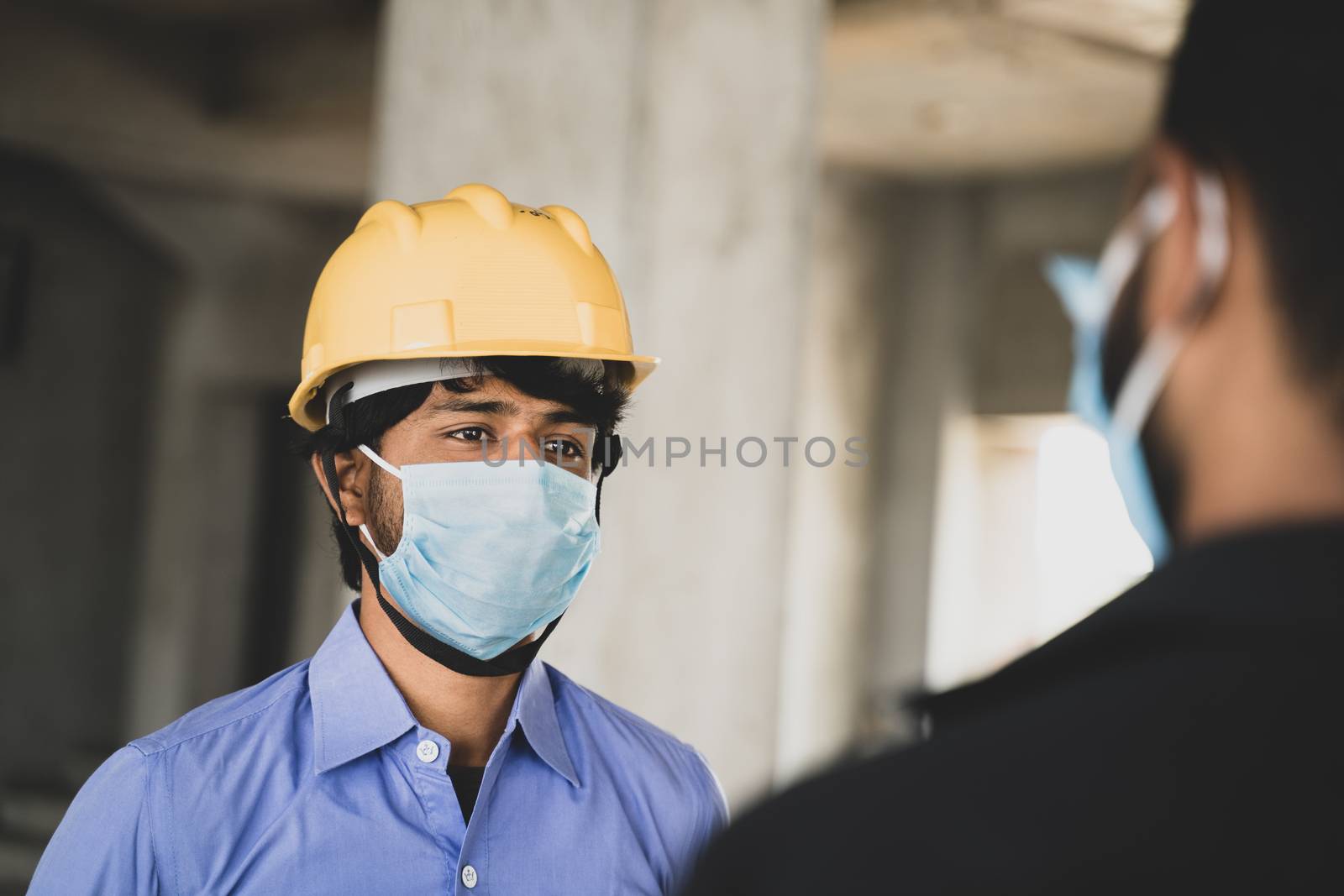 Two Construction workers or engineers at site talking by wearing medical face mask while maintaining social distance - concept of business, industry reopen or covid-19 safety measures at workplace. by lakshmiprasad.maski@gmai.com