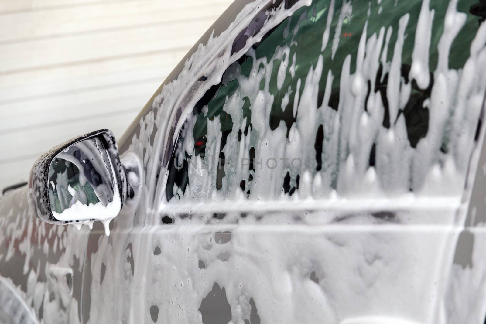 Closeup view of motor car window with layer of soap sud during car wash. Selective focus with shallow depth of field,