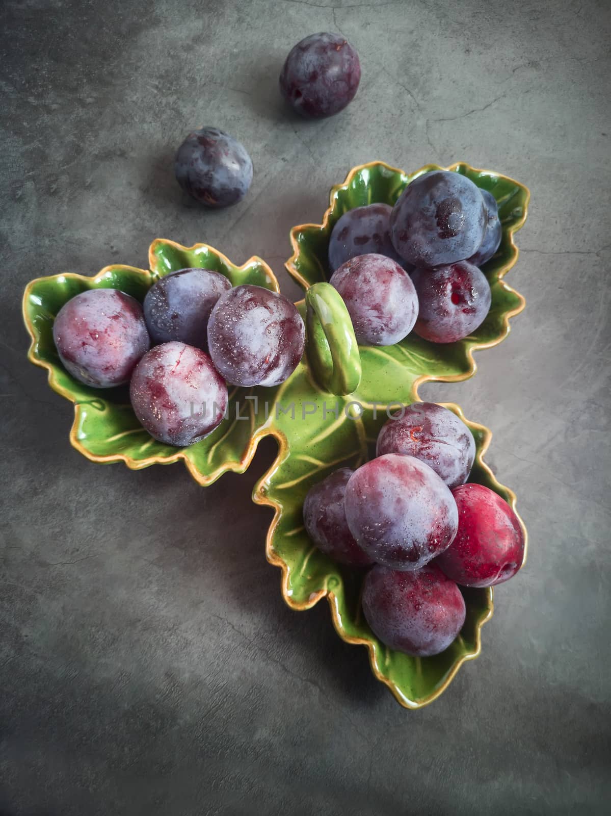On the table in a ceramic dish are large ripe plums. Presented in close-up on a dark background.
