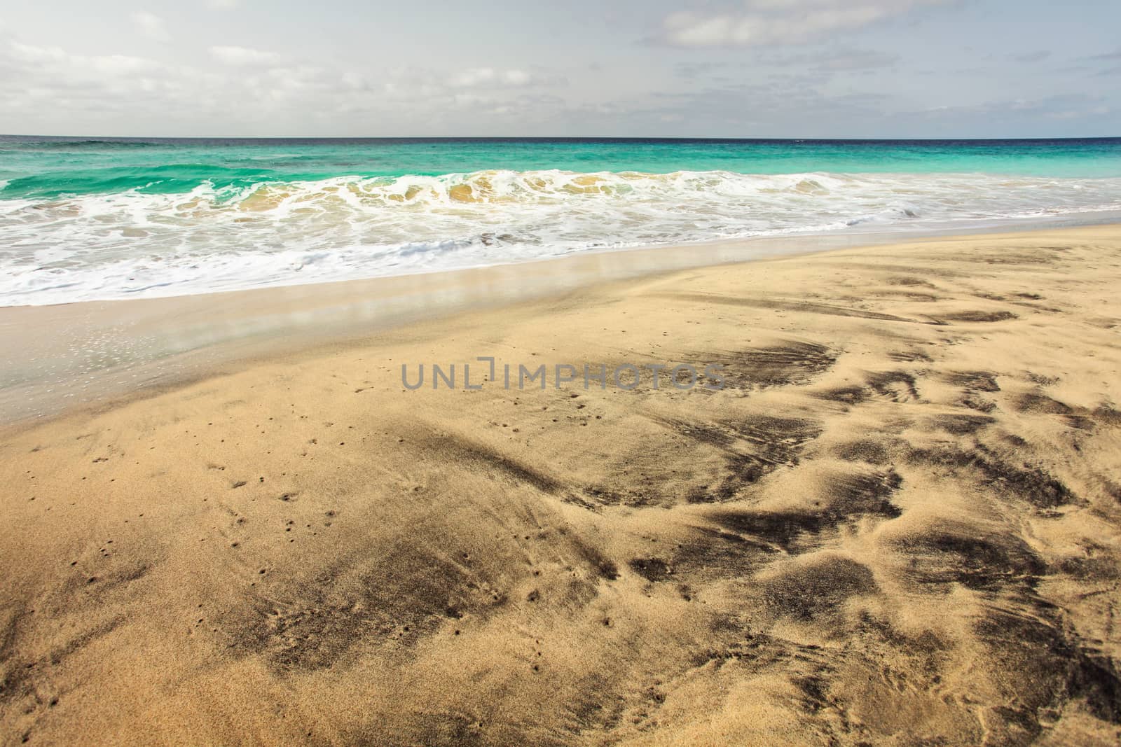 Gorgeous empty beach with golden and black volcanic spots sand, with azure sea in the background. Sal, Cape Verde