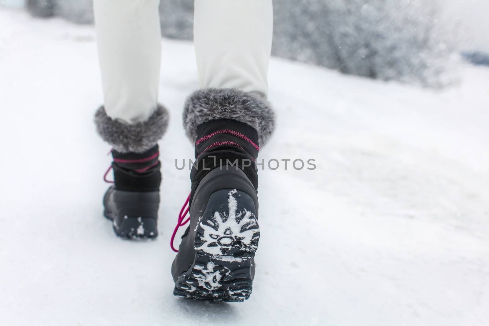 Detail of woman lifting her black and gray snow boot with faux fur and purple laces, showing tread of the boots, shot on winter overcast day.