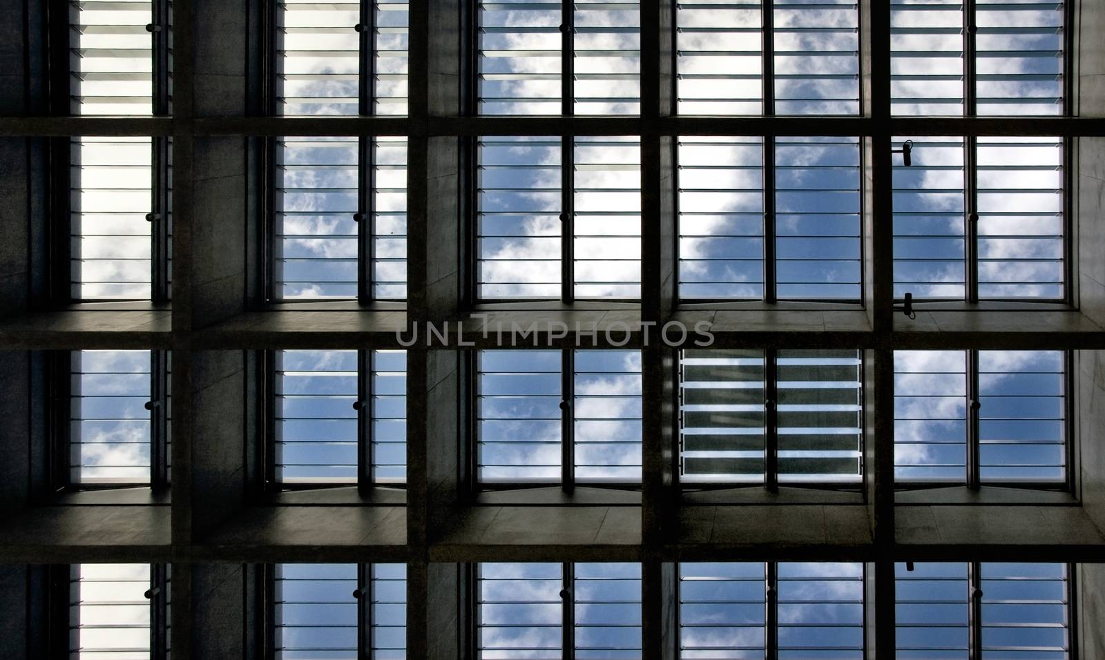 Looking up to the blue sky with clouds through roof windows with all light blinds opened but one closed.