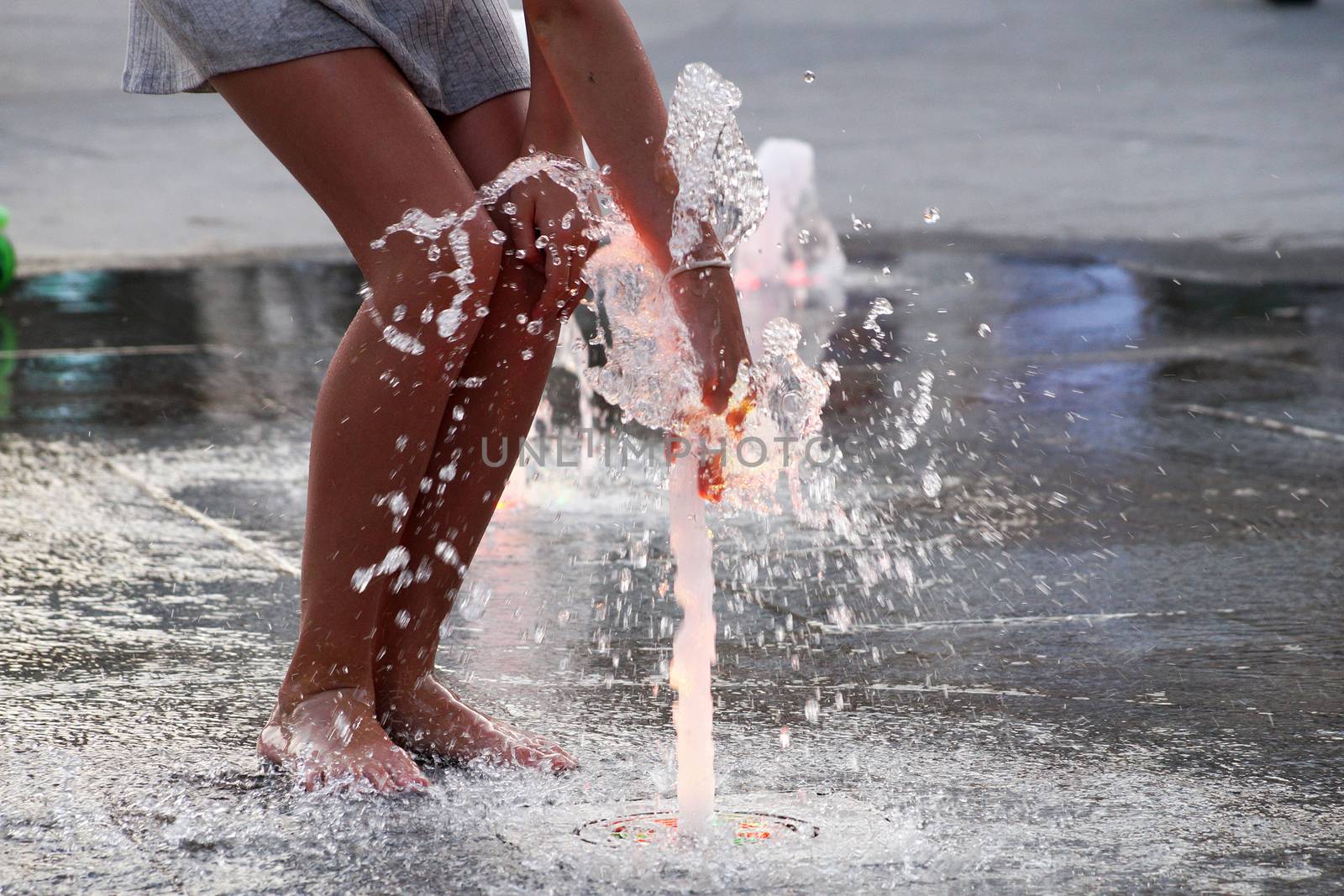 barefoot girl touching the fountain on the sidewalk by Annado