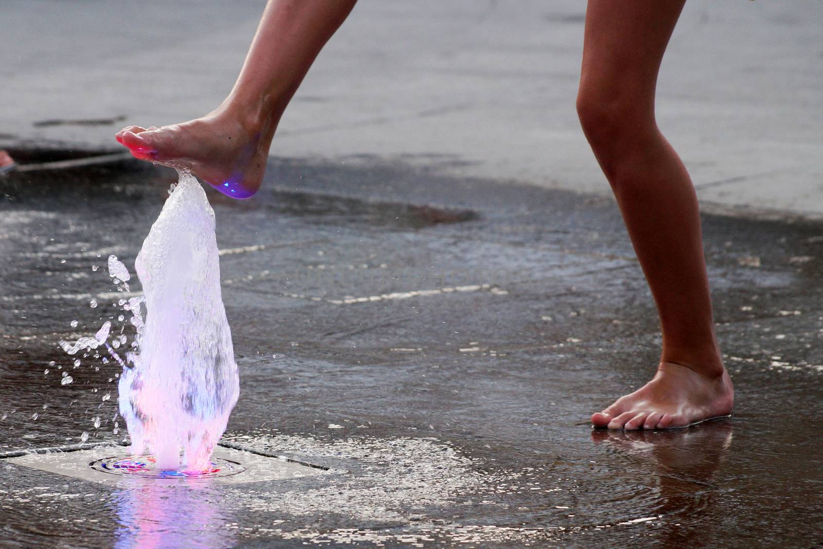 barefoot girl touching the fountain on the sidewalk in the evening