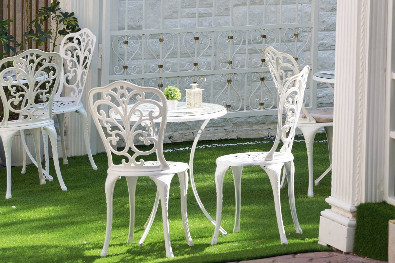 openwork white metal tables and chairs on a green lawn