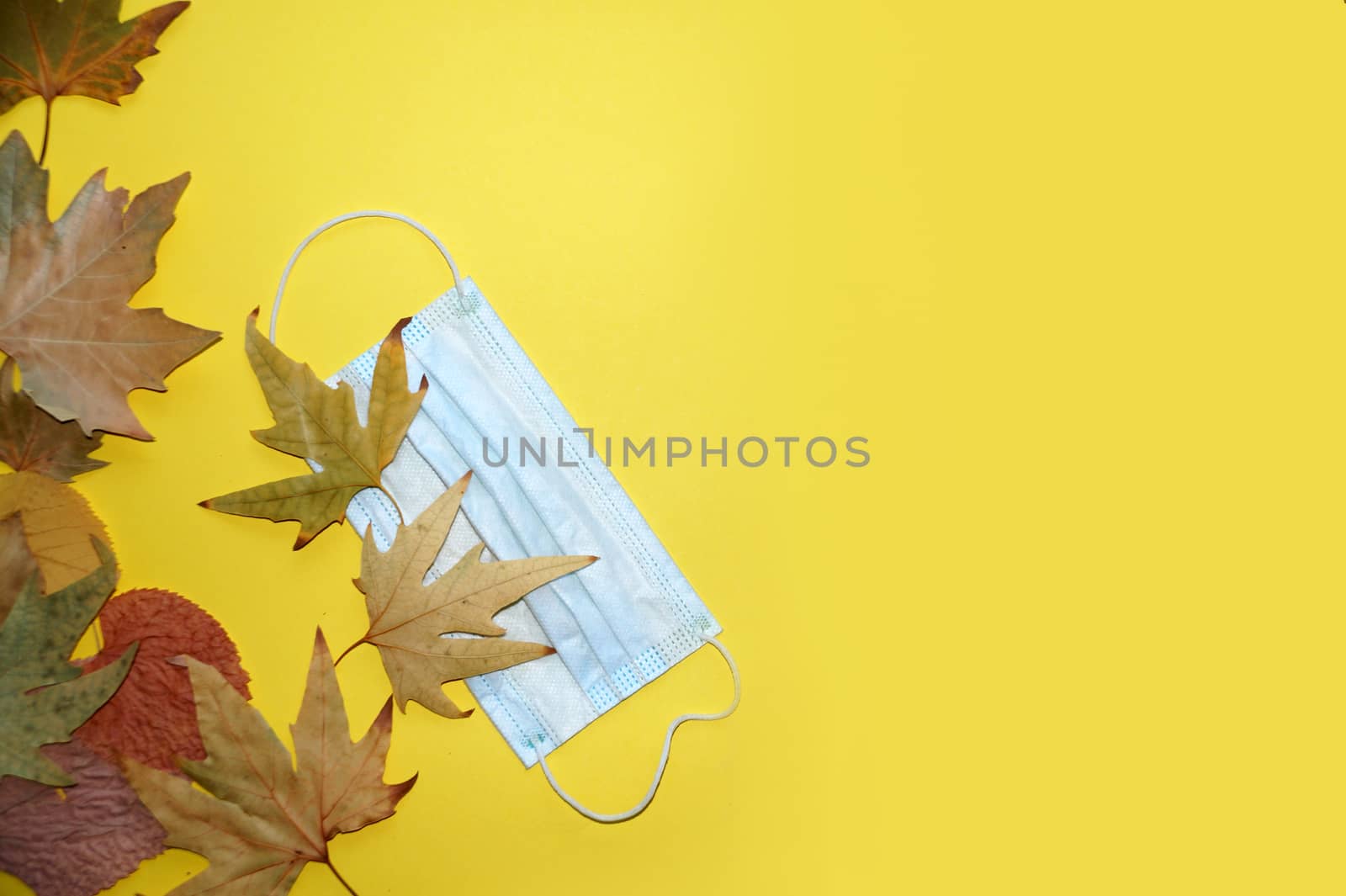 medical mask and autumn leaves on yellow background, copy space, mockup blank.