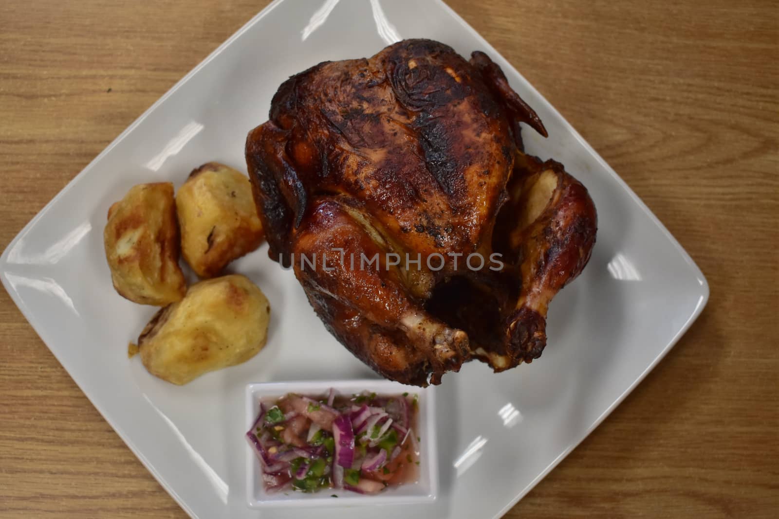 Rotisserie Chicken on a White Plate on a Wooden Table With Potatoes and a Small Salad Next to It