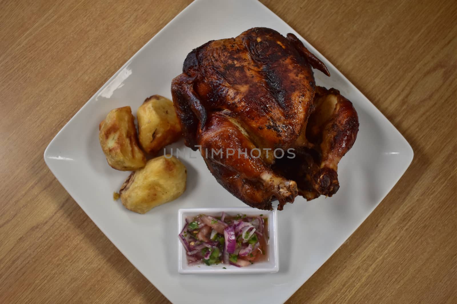 Rotisserie Chicken on a White Plate on a Wooden Table With Potatoes and a Small Salad Next to It