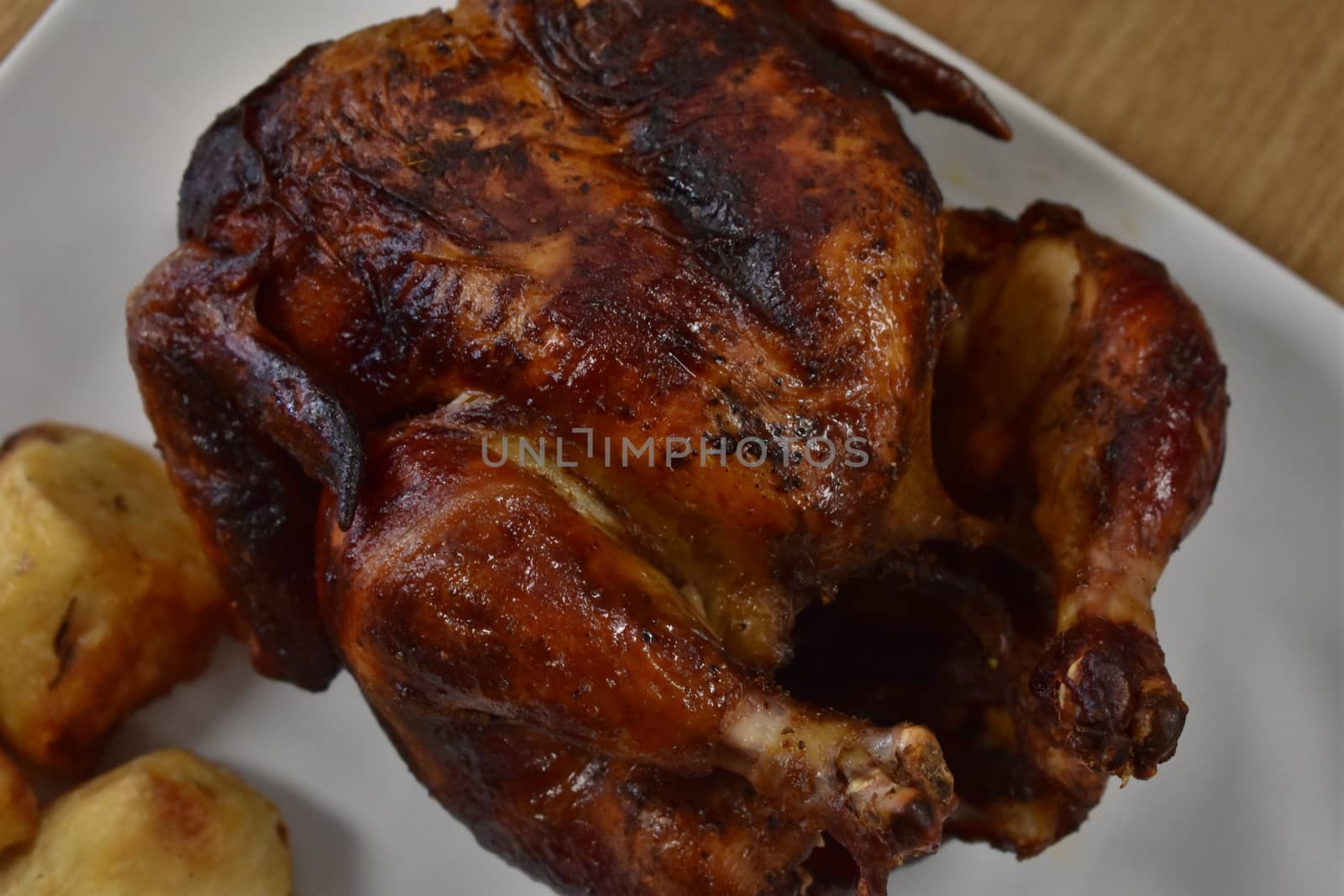 Rotisserie Chicken on a White Plate on a Wooden Table With Potatoes and a Small Salad Next to It