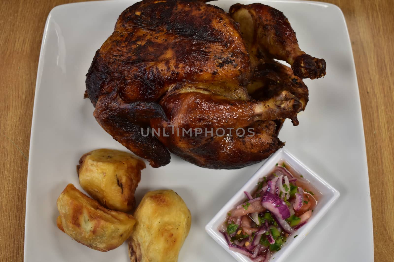 Rotisserie Chicken on a White Plate on a Wooden Table With Potatoes and a Small Salad Next to It