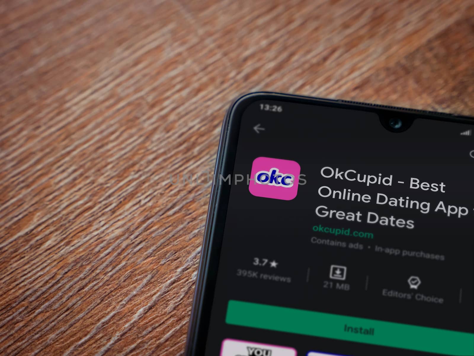 Lod, Israel - July 8, 2020: OkCupid app play store page on the display of a black mobile smartphone on wooden background. Top view flat lay with copy space.