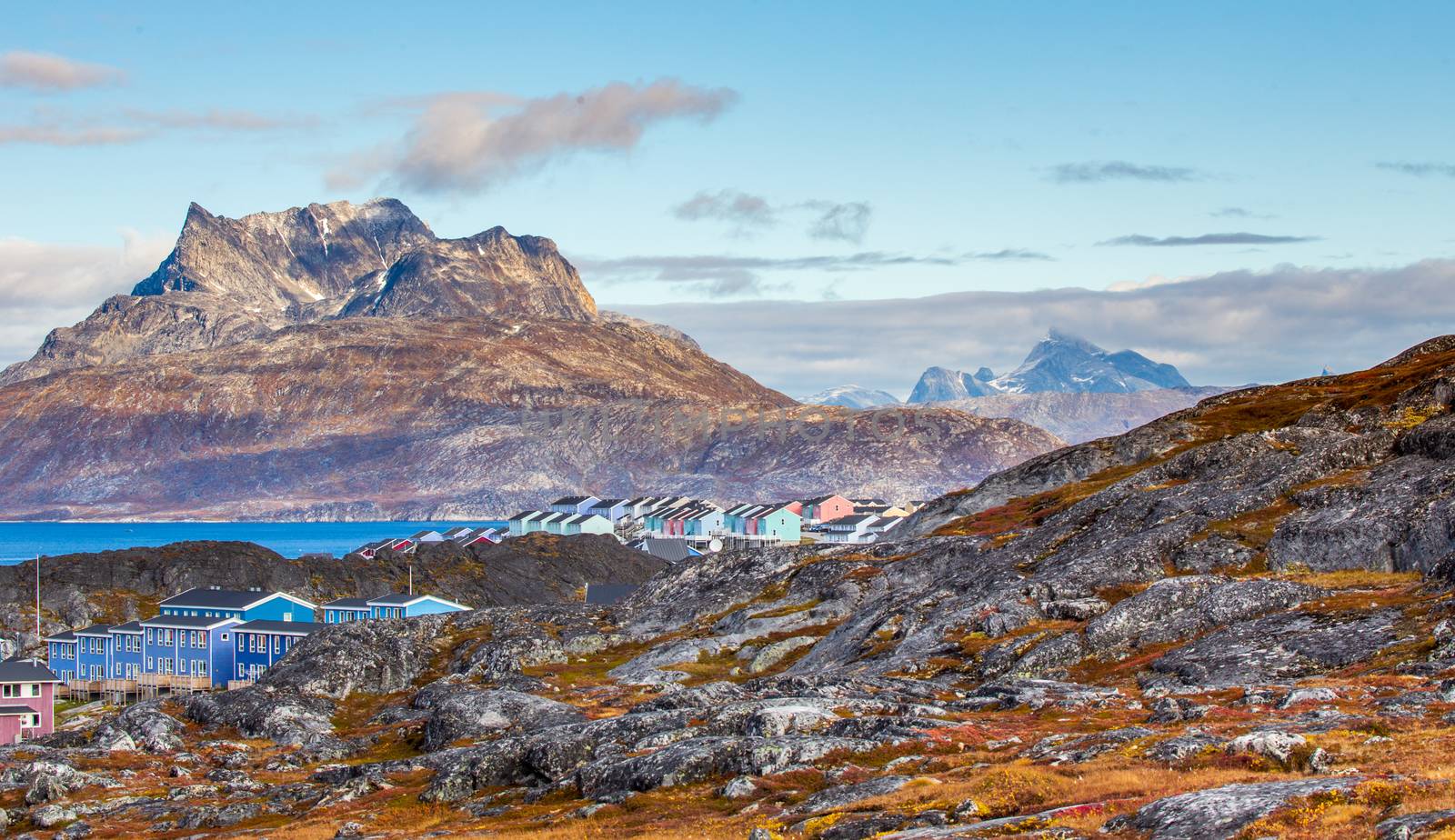 Inuit houses and cottages scattered across tundra landscape in residential suburb of Nuuk city with fjord and mountains in the background, Greenland
