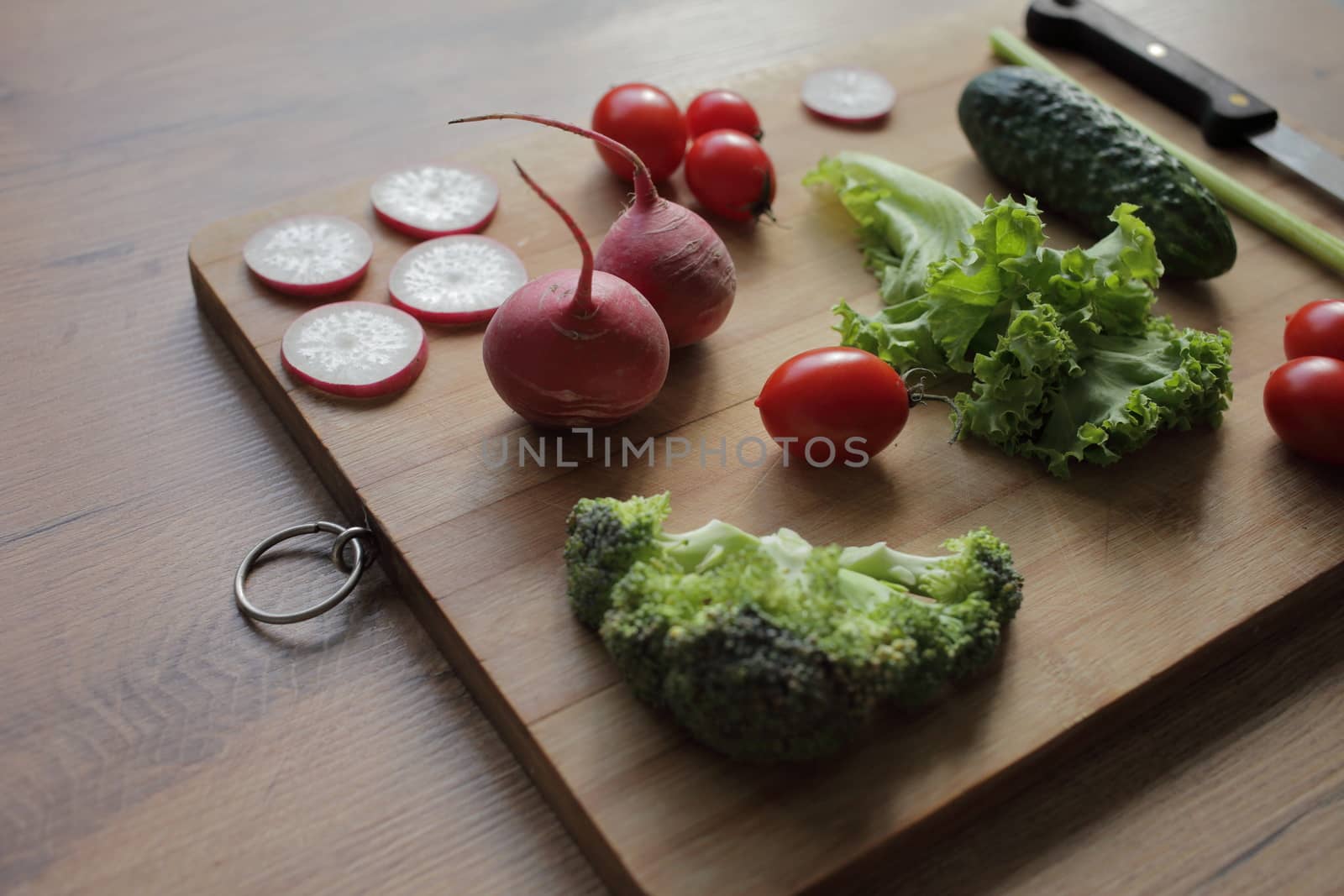 Fresh vegetables on a cutting board on a wooden table Tomatoes, cucumber, lettuce, broccoli, radish, knife