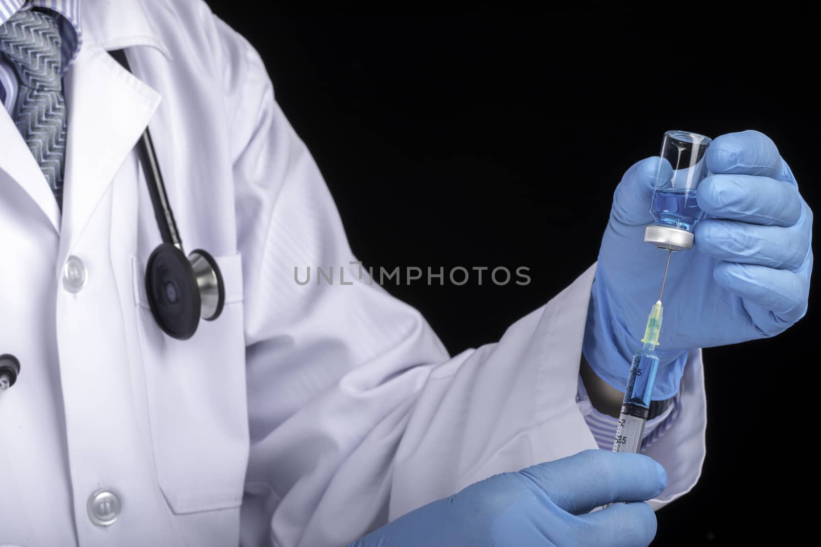 A doctor in white coat drawing clear light blue liquid from a vial into a syringe. Medication or vaccine adminstration, covid-19 prevention concept. Dark background.