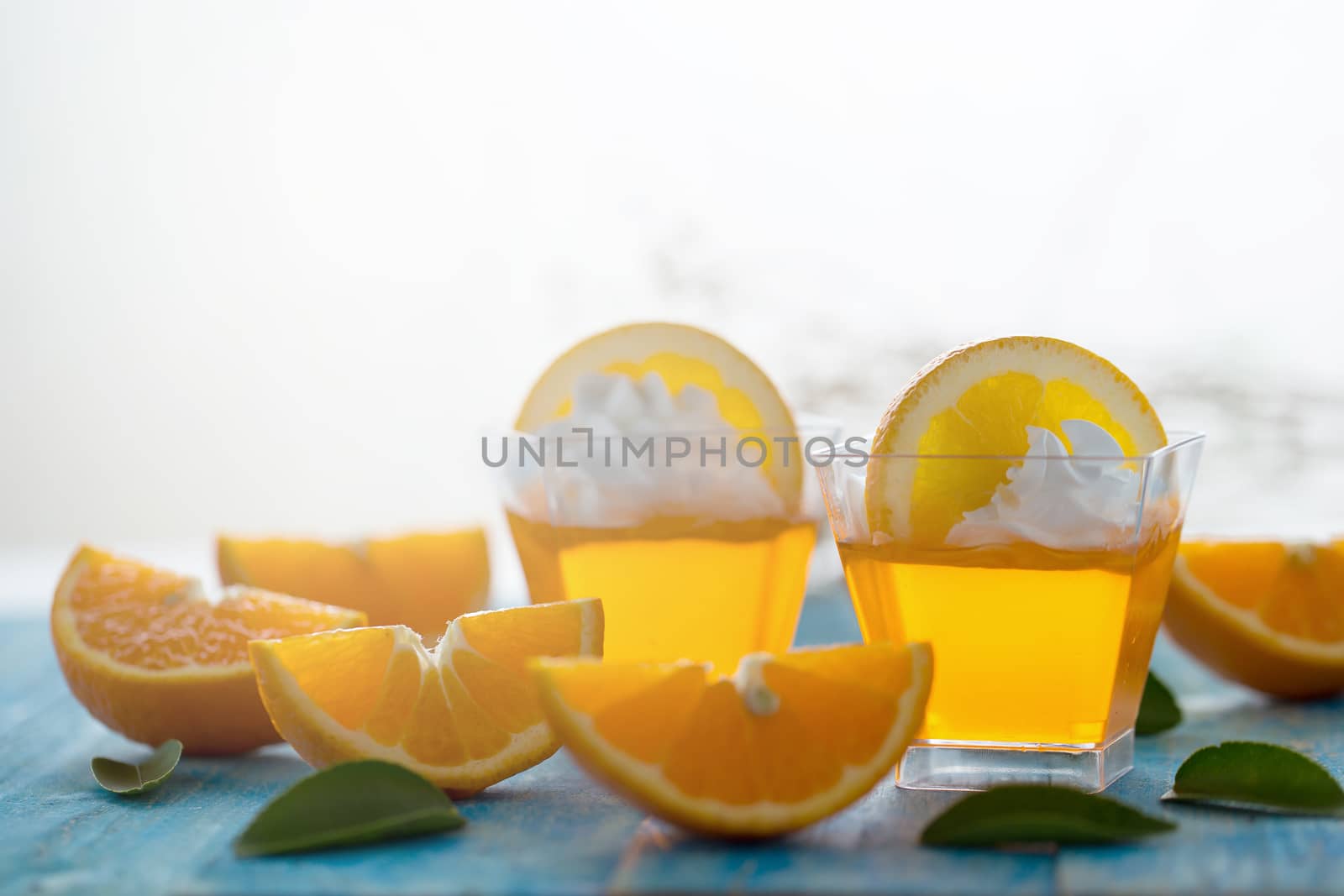 Orange jelly in a cup with whipped cream and orange sliced on blue wooden background.