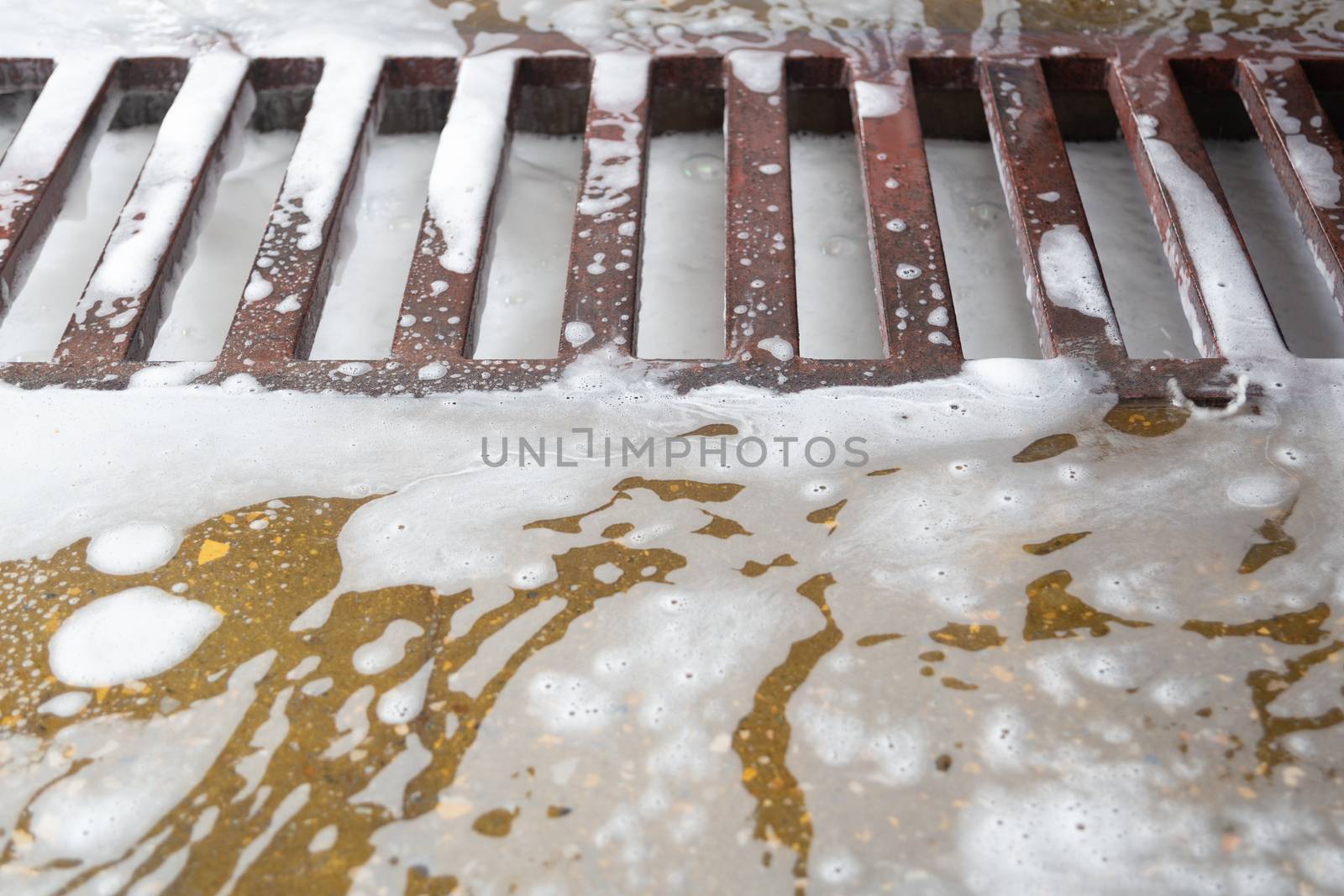 Floor grid with soap sud waste in car washing garage. Full frame close-up with selective focus and blur.