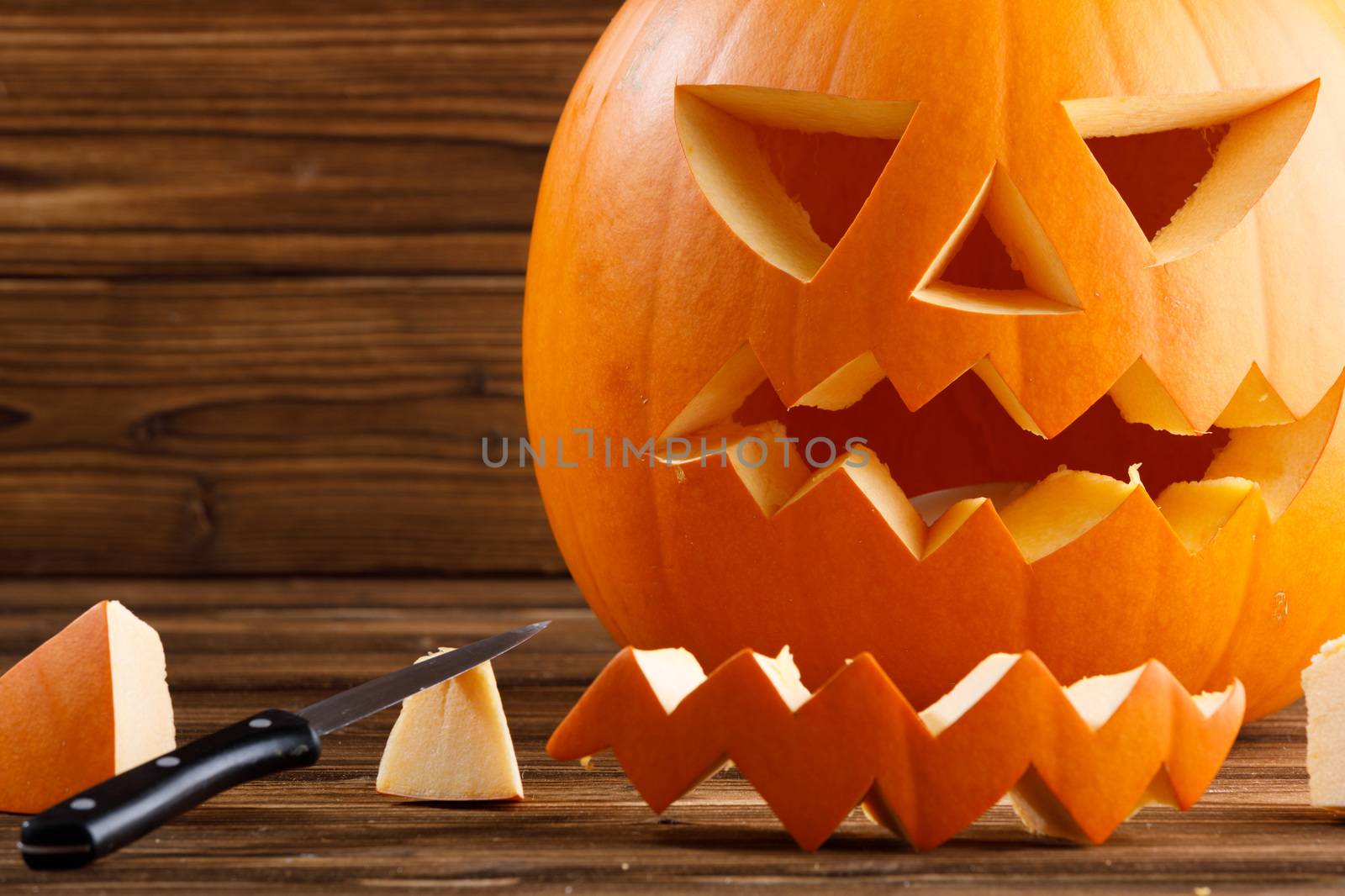 Carving of Halloween pumpkin in progress, pieces and cutting knife on wooden background