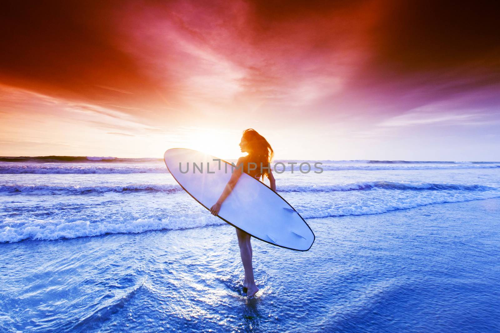 Beautiful mixed race woman on tropical beach holding surfboard at sunset