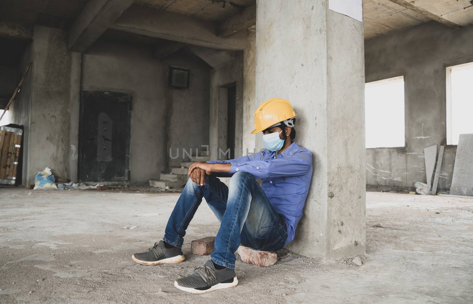 construction worker sitting sad and lonely at job site wearing a medical mask with hardhat to prevent Covid-19 spreading, Concept of unemployment, economic crisis Job loss during coronavirus crisis