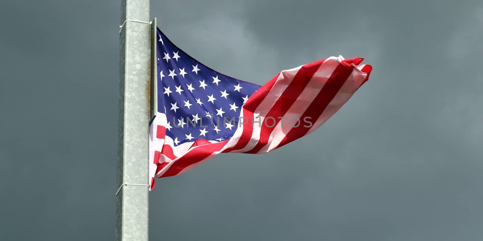 USA flag at a flagpole moving in the wind against the sky