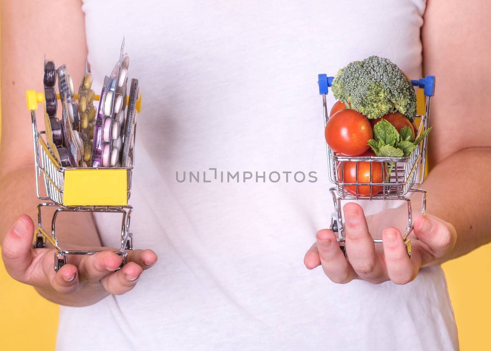 Hands holding shopping carts with vegetables and tablets on a yellow background, the concept of choosing healthy food and disease