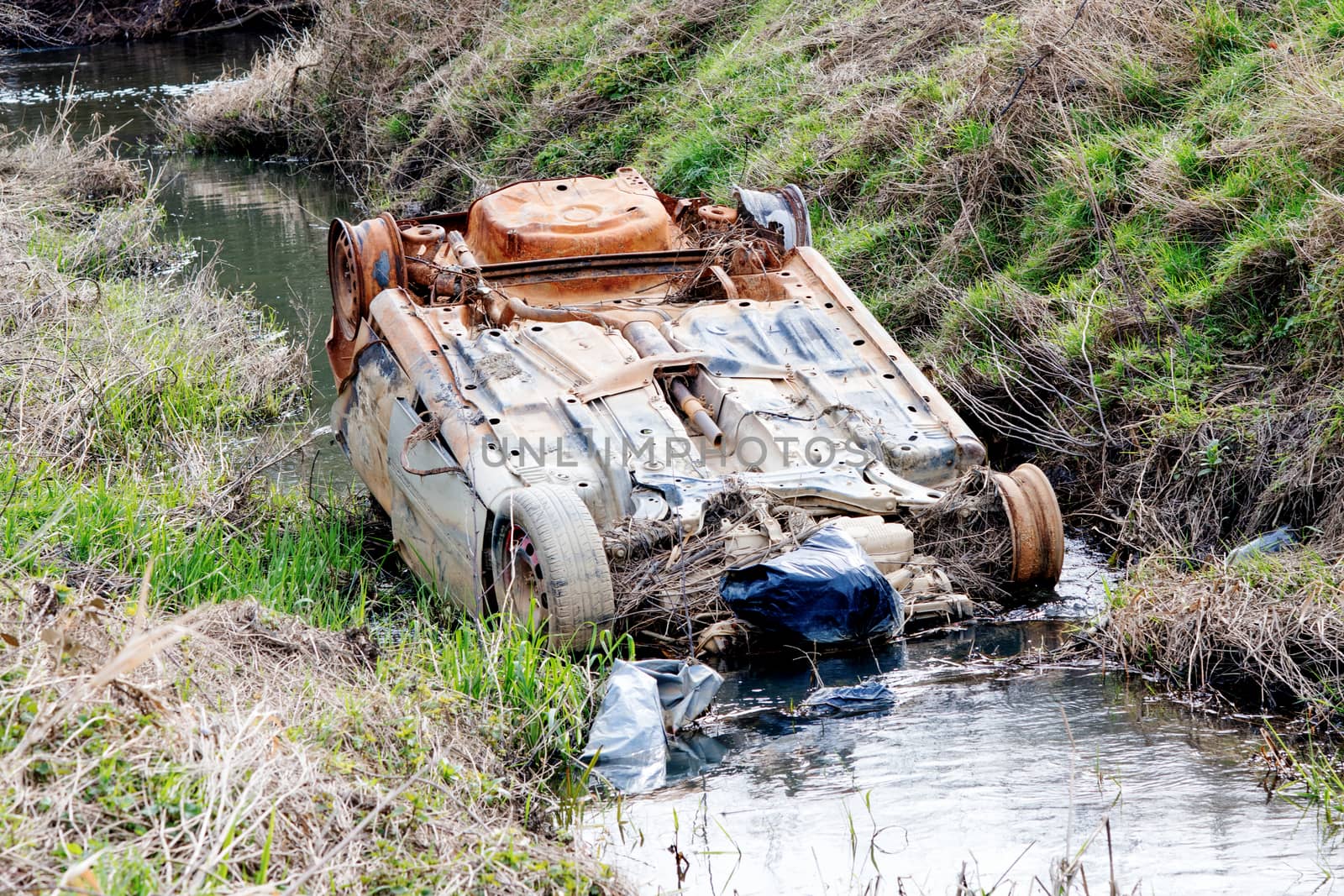 Stolen burnt rusty car abandoned in a river in the countryside polluting the environment