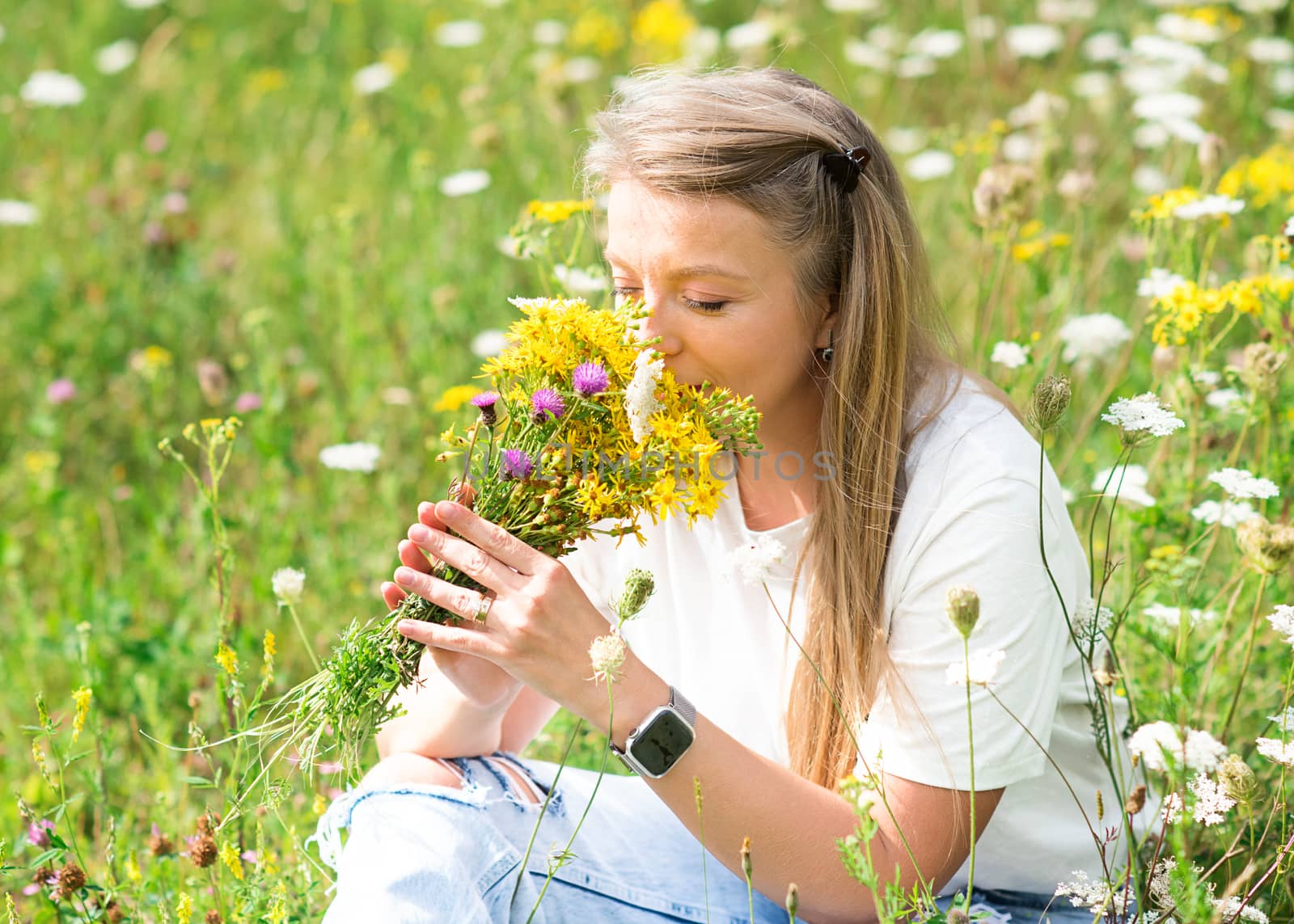 a woman holding a posy and sniffing flowers on a meadow in the afternoon