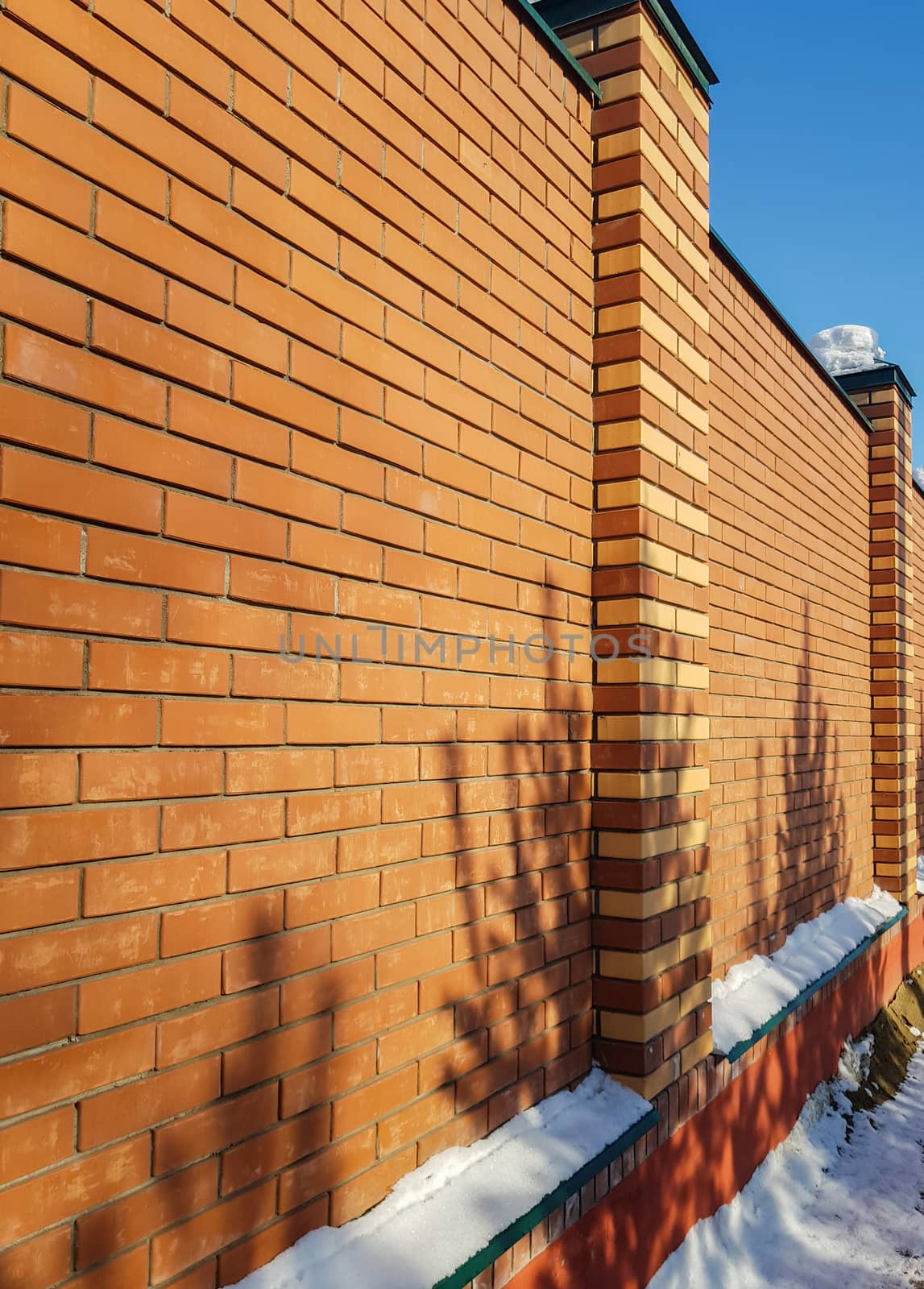 Modern red brick fence with turrets, in winter, outdoors.