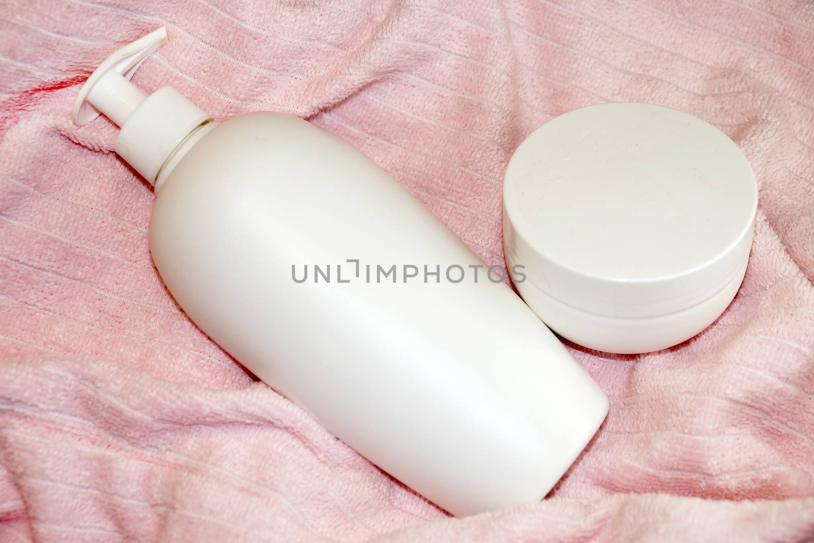 white cosmetic bottle and cream jar on pink terry cloth close-up