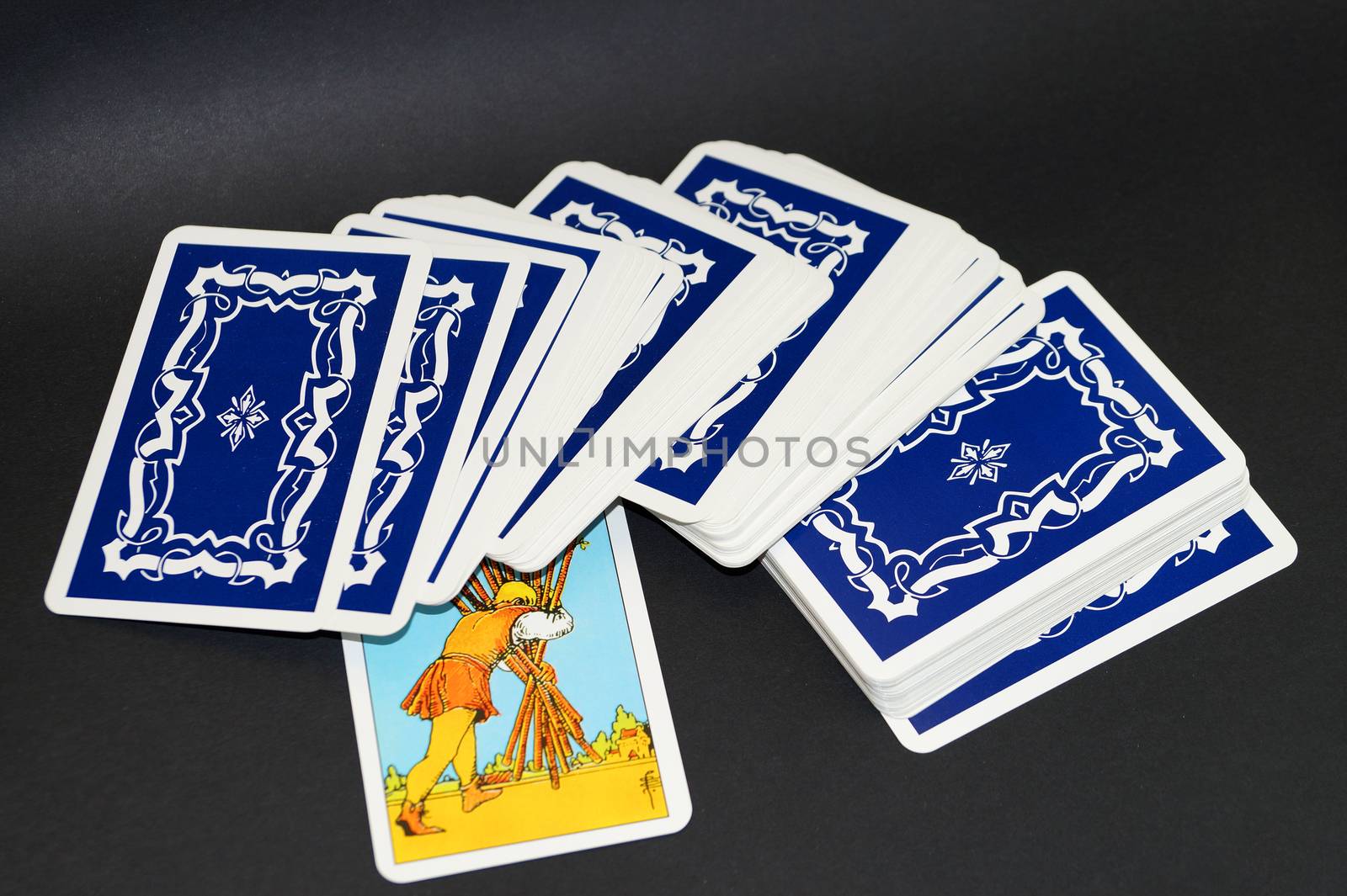 scattered deck of tarot cards with one card upside down on black background by Annado