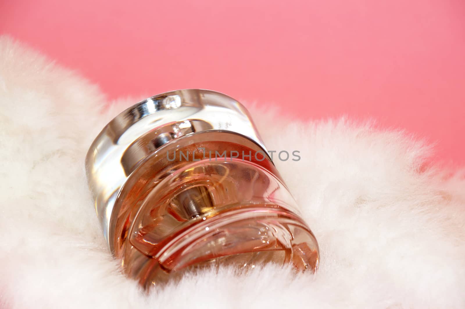 perfume bottle and white fur on a pink background close-up