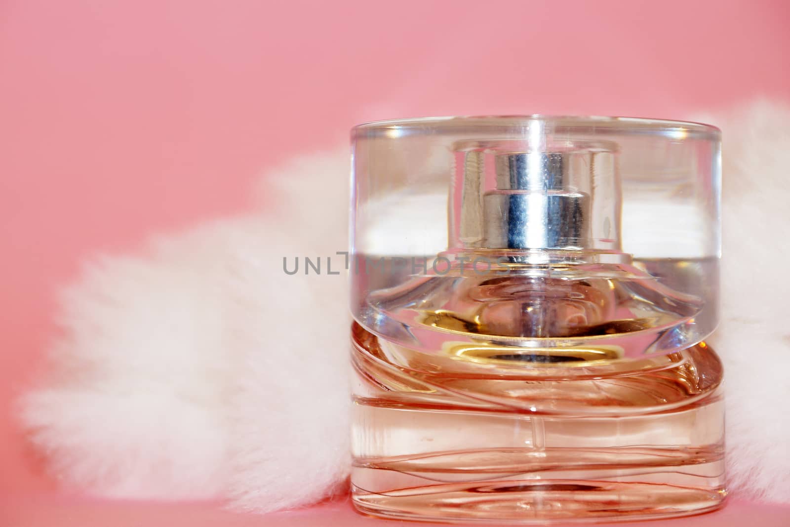 perfume bottle and white fur on a pink background close-up