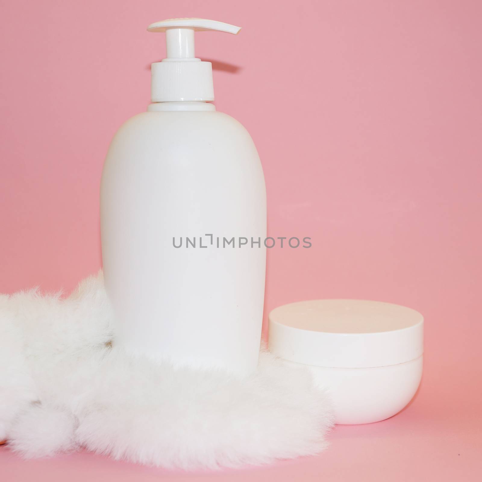 white cosmetic bottle, cream jar and white fur on pink background by Annado