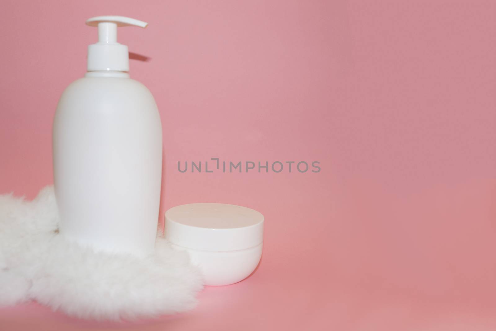 white cosmetic bottle, cream jar and white fur on pink background by Annado